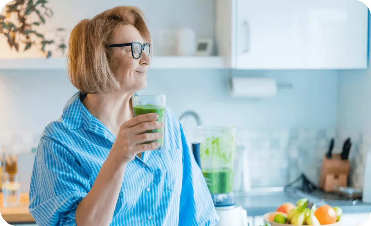 An elderly woman holding a transparent glass with green health juice