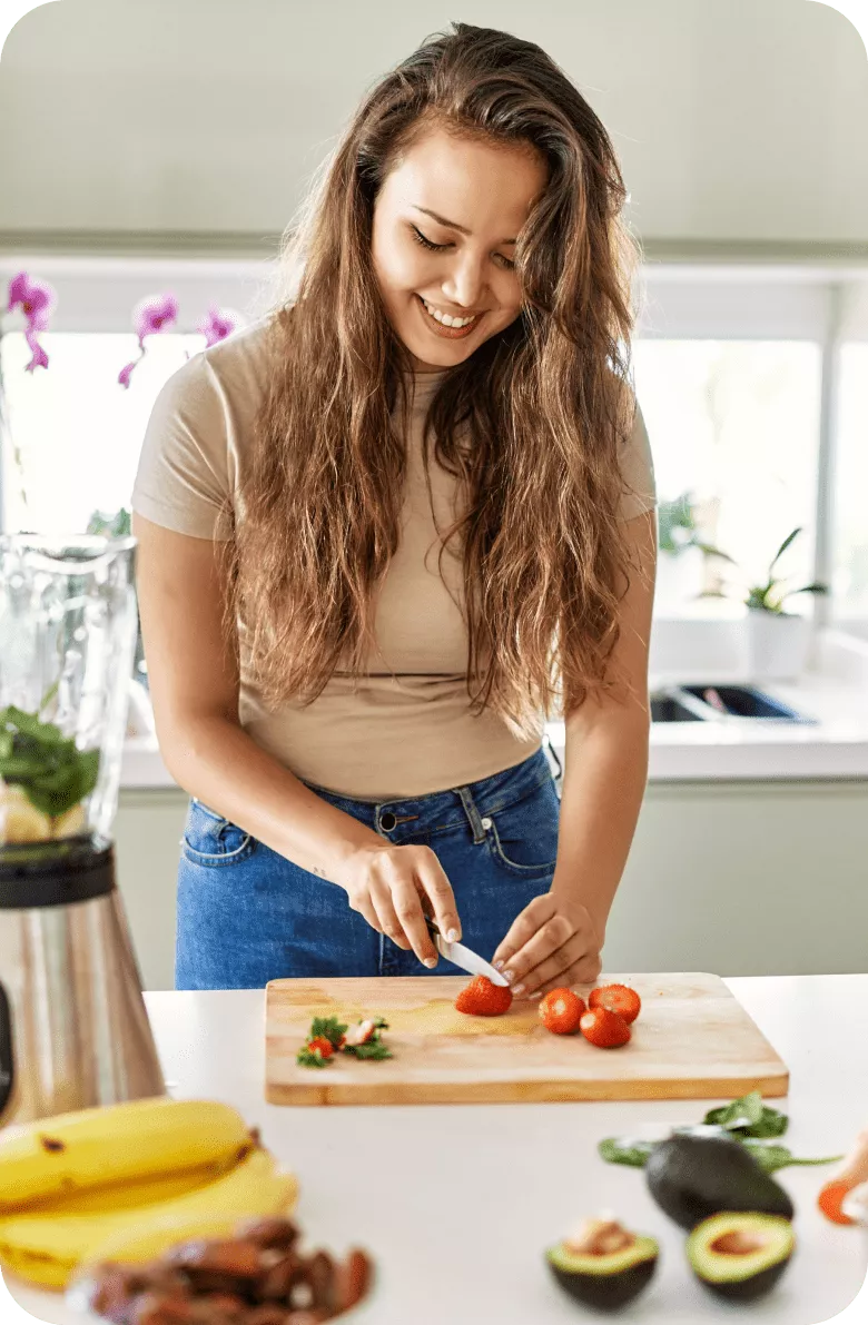 A smiling woman cutting tomatoes on a cutting board in the kitchen